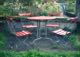 A0434 – Roter Gartentisch mit 4 Stühlen, Nutzgarten im Hintergrund